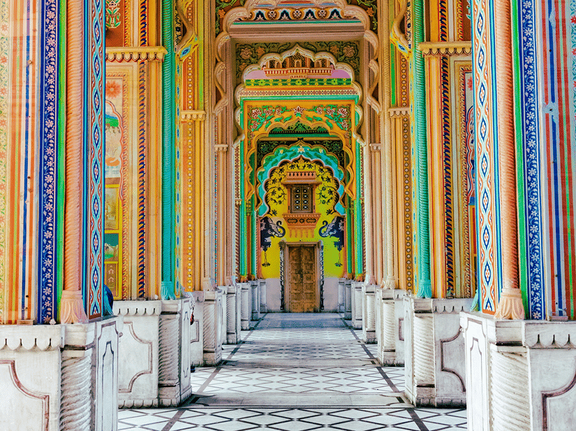 Perspective view down a bright palace corridor decorated with vibrant pastel arches and tiled floors.