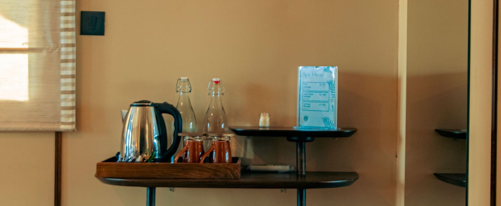 A corner with mounted lamp, a table with kettle, cups, and bin below at Fireflies Resorts, Kabini.