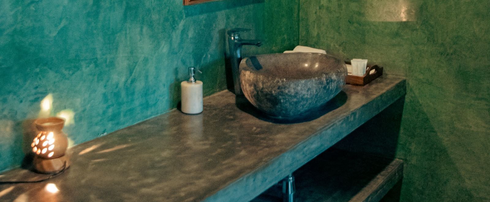 Bathroom with green walls, a vessel sink, mirror, and toiletries on a stone counter at Fireflies Resorts, Kabini.