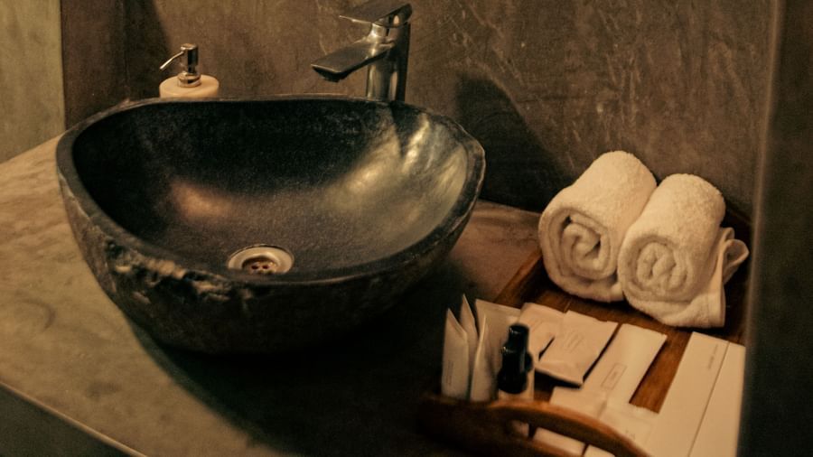 Bathroom with black stone basin, rolled towels, and mirror at Fireflies Resorts, Kabini.