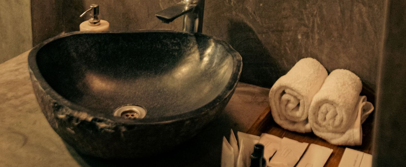Bathroom with black stone basin, rolled towels, and mirror at Fireflies Resorts, Kabini.