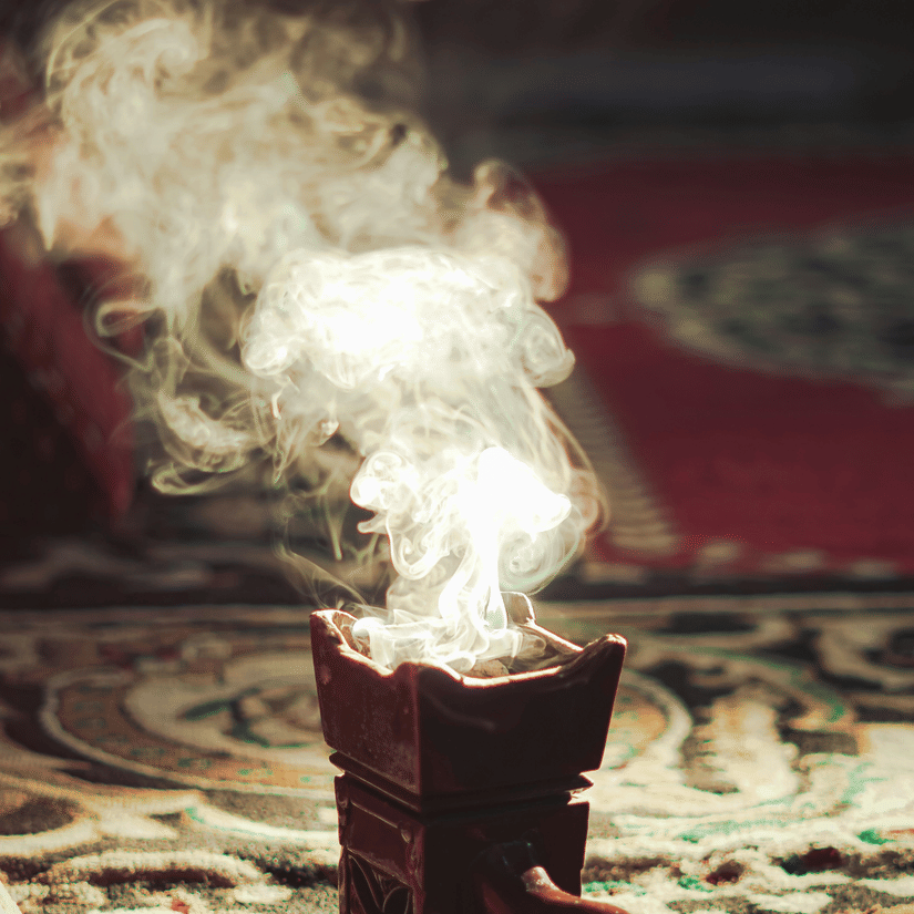 An overview of a device with smoke coming out of it, caused by a lit Oud, that is kept on on rug inside a living room of a house.