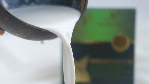 a close up shot of a person pouring coconut milk inside a cup 
