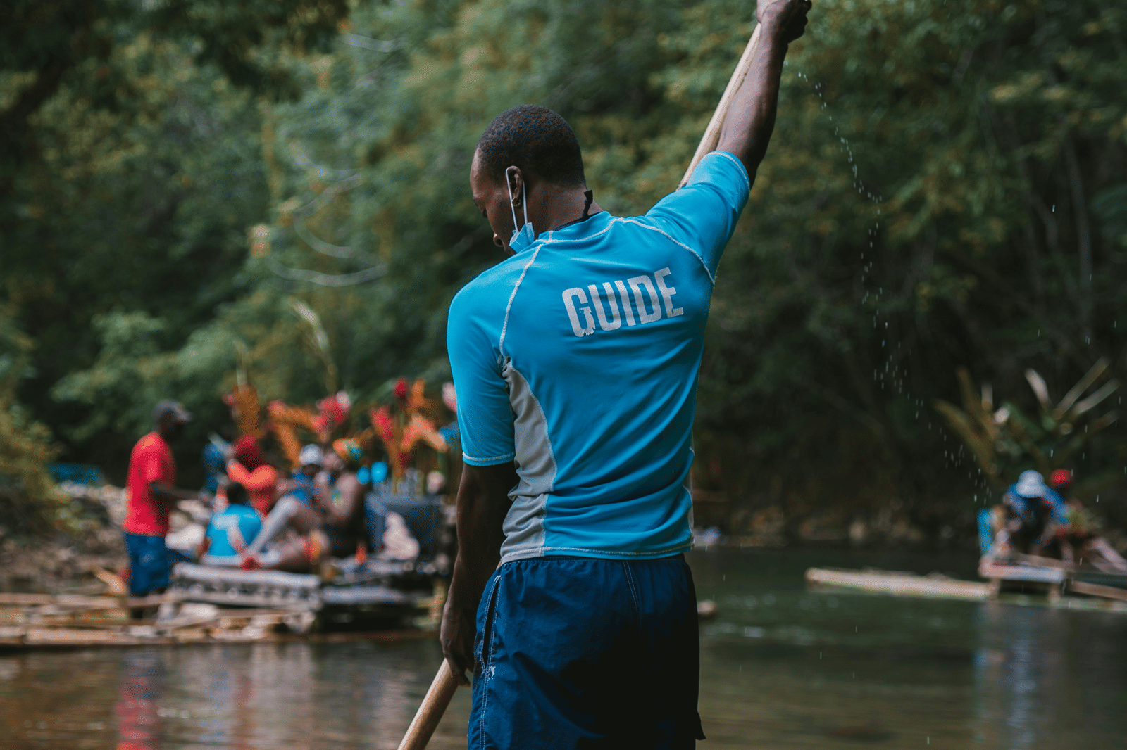 A person using a bamboo raft in a river with other bamboo rafts seen in the distance.