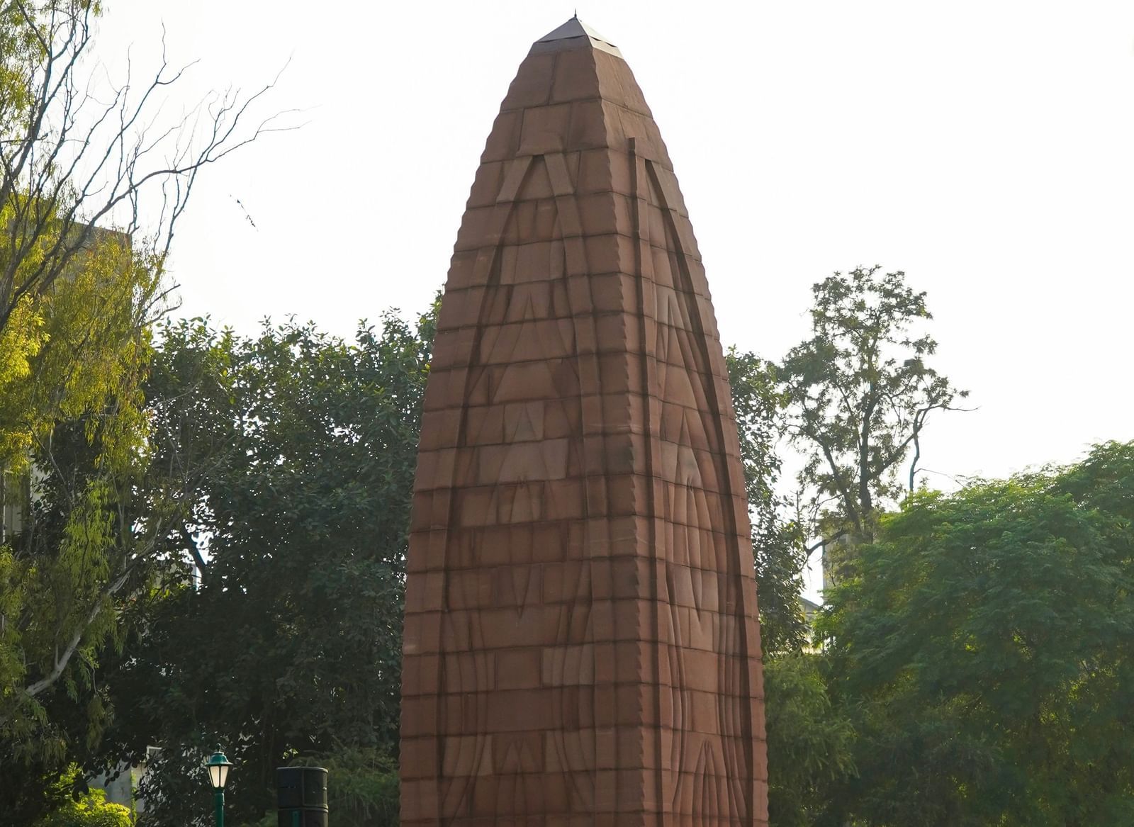 Monument with a distinct bullet-like shape made of red sandstone, set in a green parkland.