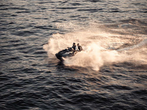 Two people enjoying a jet ski ride across the sea, creating a trail of spray during an exciting water sports adventure.