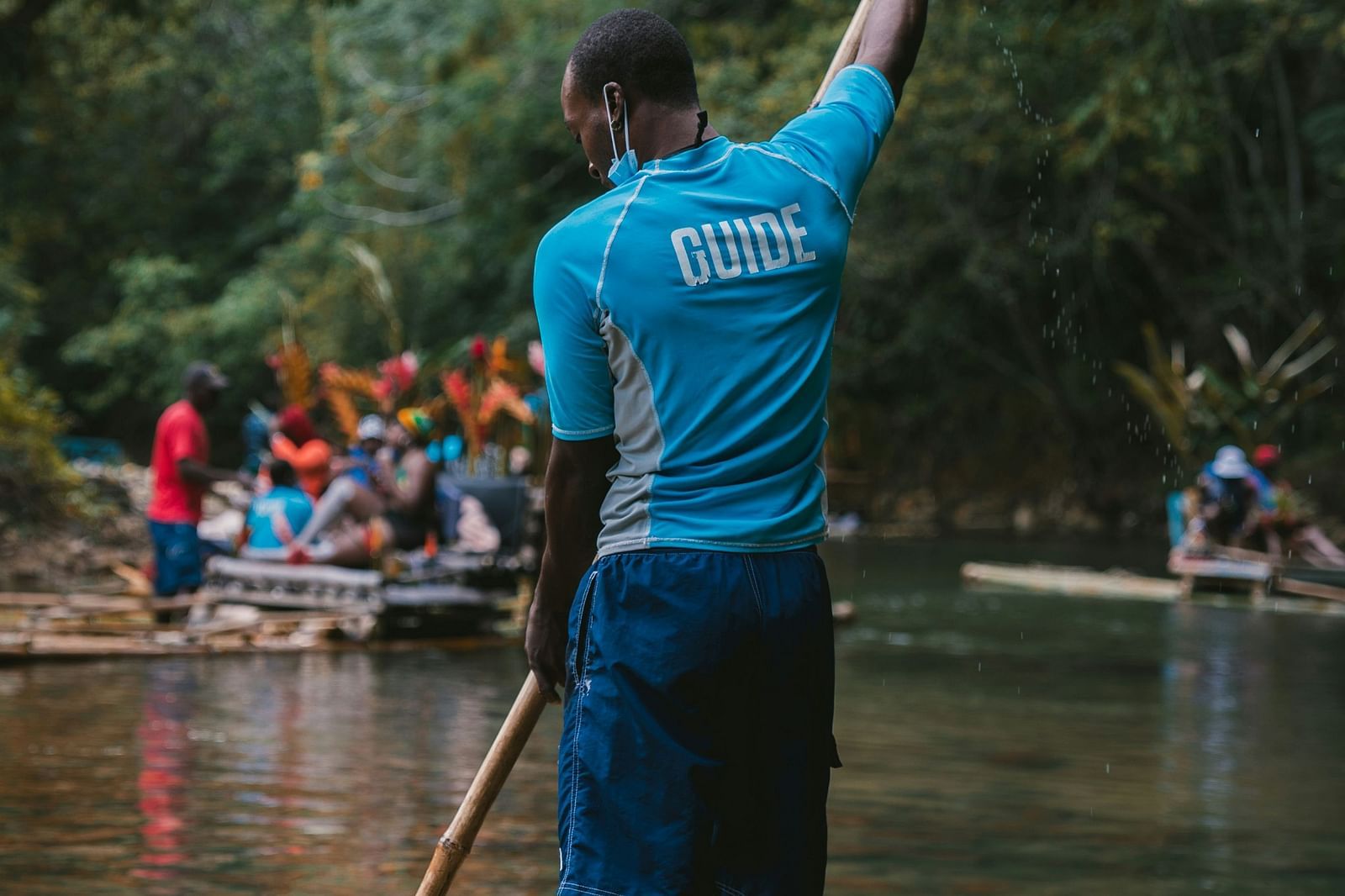A person using a bamboo raft in a river with other bamboo rafts seen in the distance.