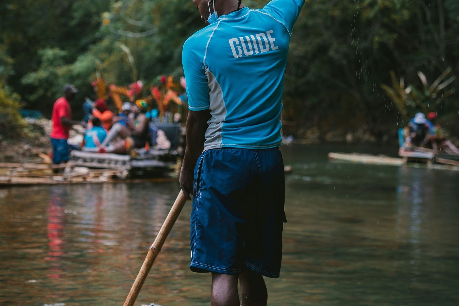 A person using a bamboo raft in a river with other bamboo rafts seen in the distance.