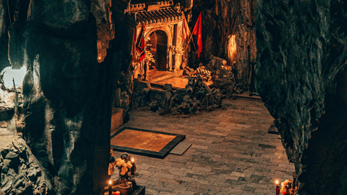 The interior of a natural rock cave used as a small shrine with orange decorations and low lighting at Ananta Express, Katra.