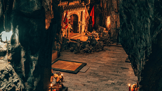 The interior of a natural rock cave used as a small shrine with orange decorations and low lighting at Ananta Express, Katra.