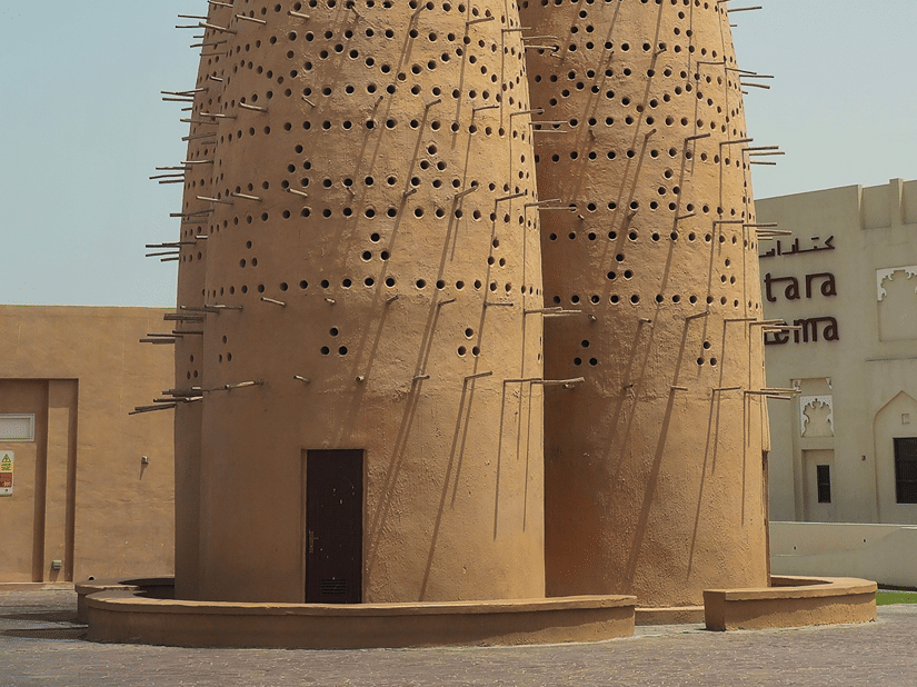 Two traditional tall mudbrick pigeon towers stand side by side under a clear blue open sky.