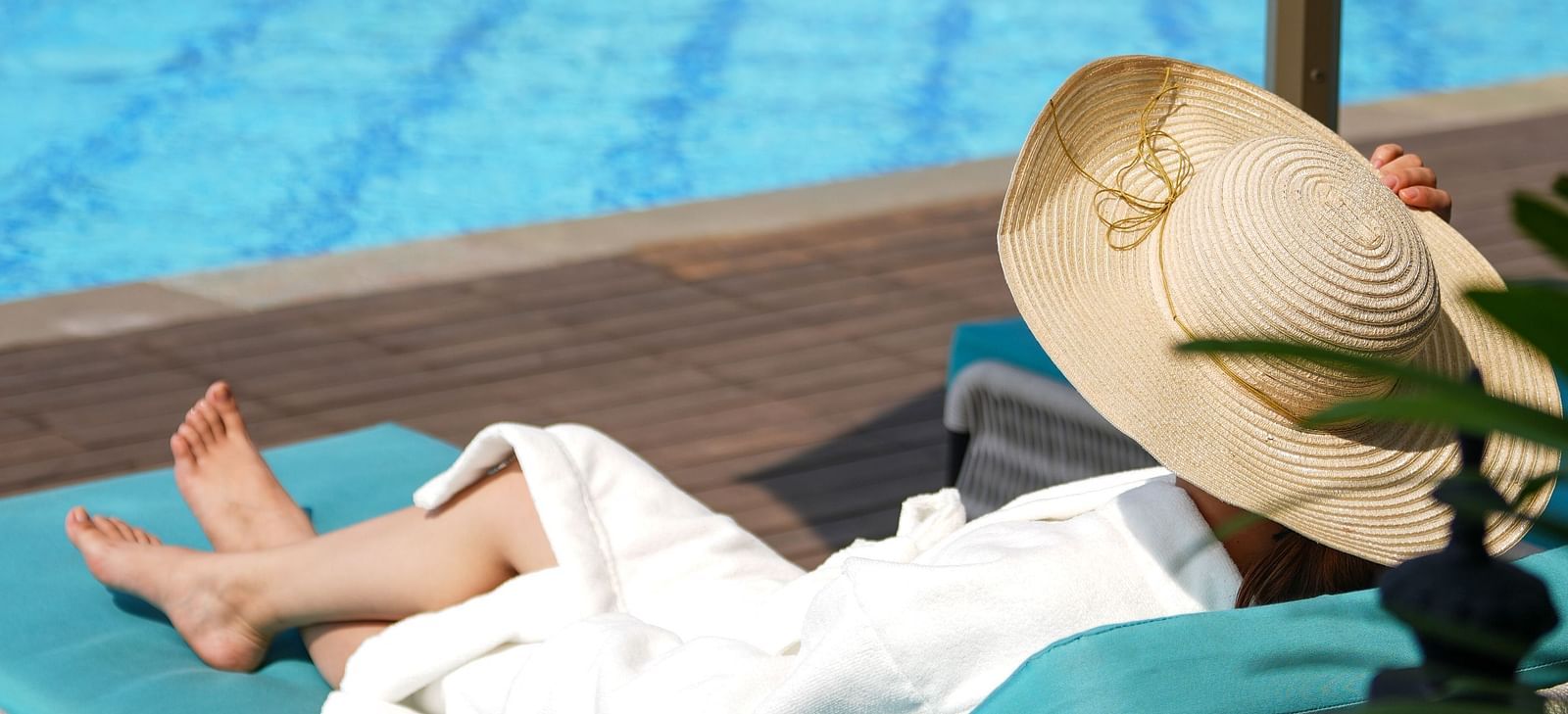 A woman dressed in a white bathrobe wearing a wide hat on her head lying on the sun lounger by the pool at Imperial Goa.