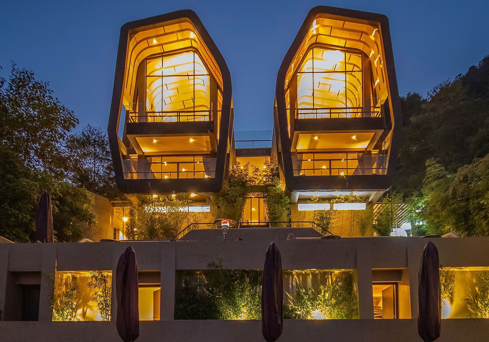 Modern hotel with illuminated rooms at night, featuring unique architectural design, reflected in a pool.