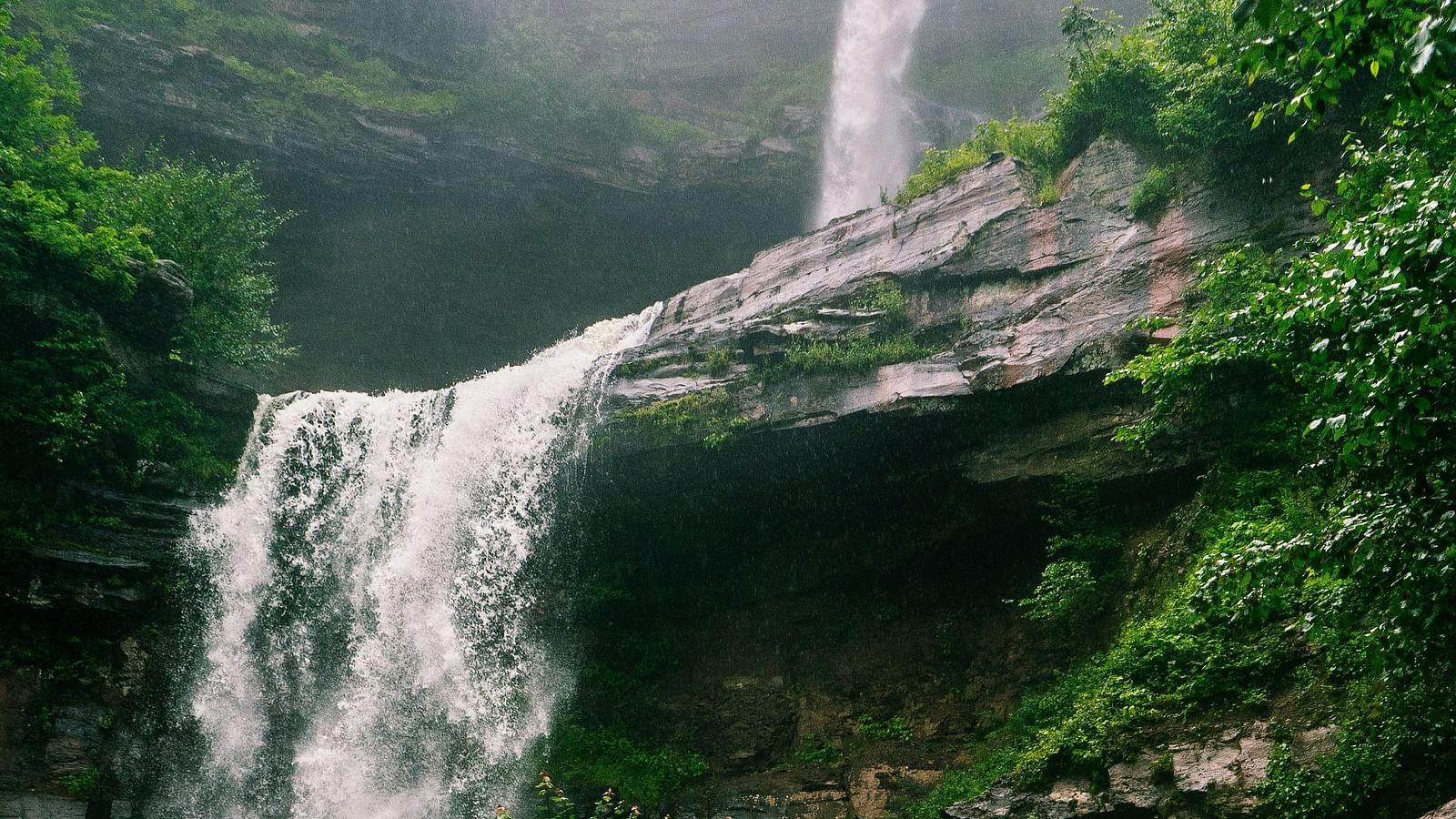 Scenic waterfall cascading over mossy rocks surrounded by lush greenery.