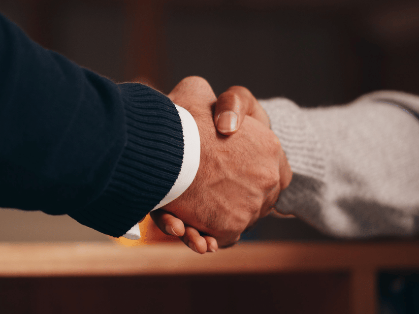 A close-up shot of 2 people engaging into a handshake.
