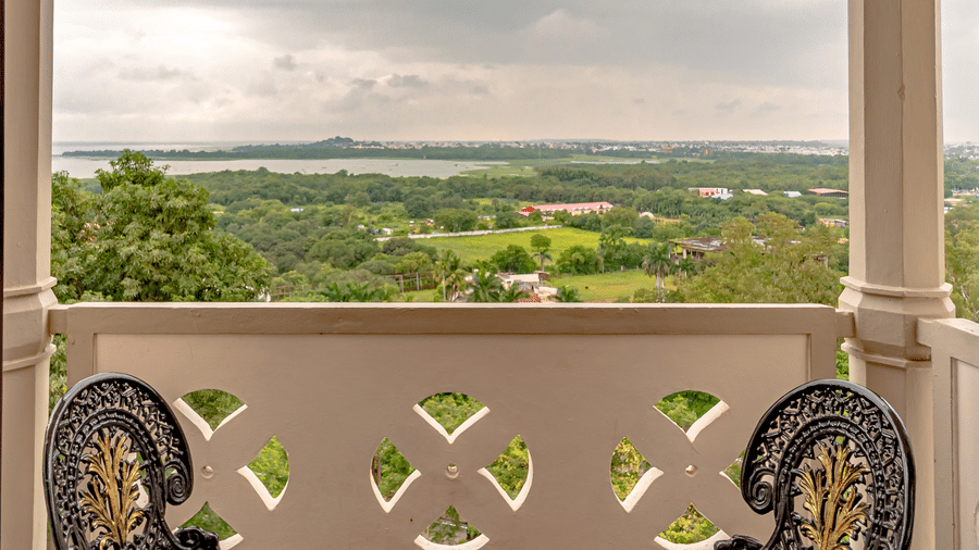 The outdoor seating area for 2 at the verandah of the Royal Club Room, overlooking the vast green landscapes under a cloudy sky at Noor-Us-Sabah Palace, Bhopal.