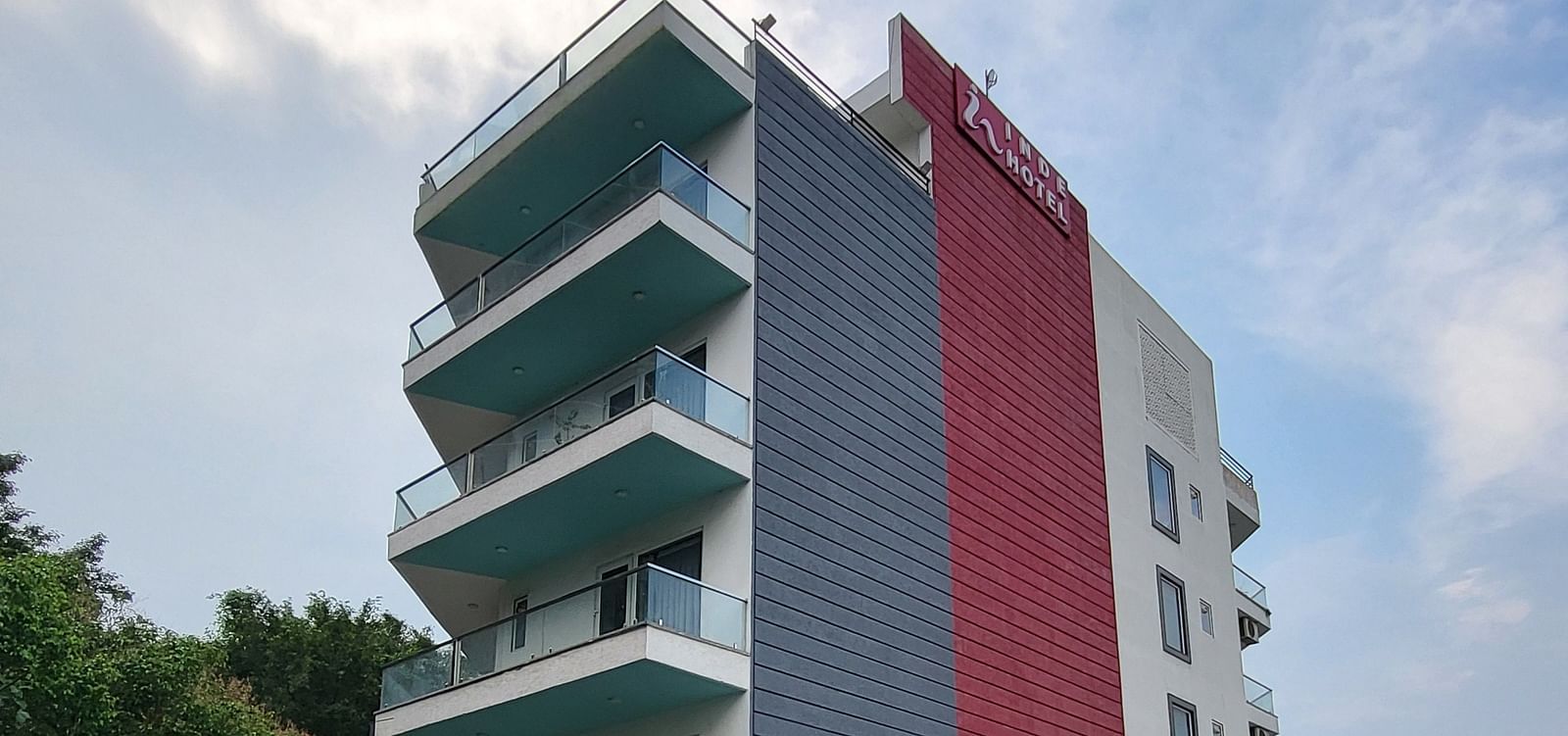 A facade of Inde Hotel Golf Course Extension featuring multiple storeys and balconies on each floor, and cars parked on the lawn