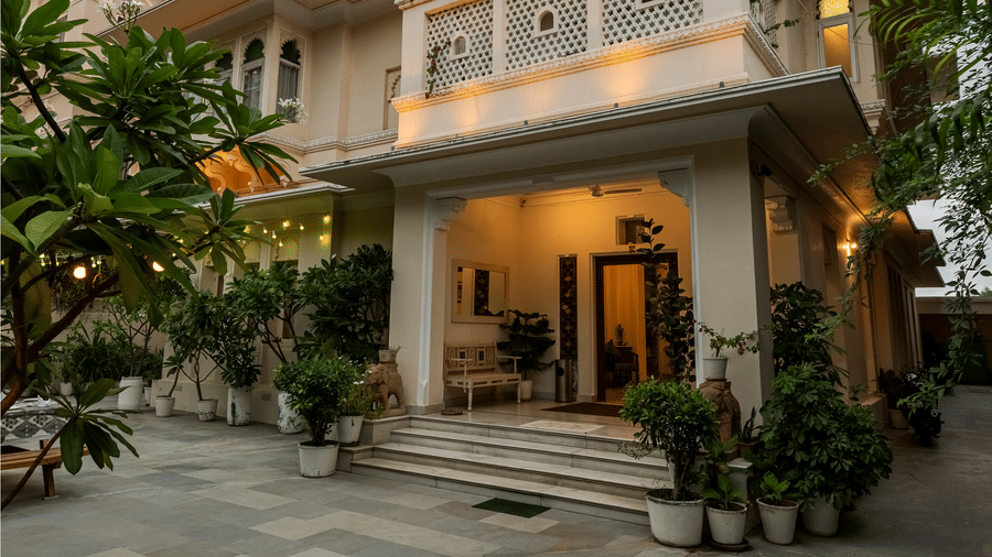 A facade of a multi-story traditional building with balconies and an entryway, with a paved courtyard at Akshay Niwas Boutique Hotel by Amantra, Udaipur.