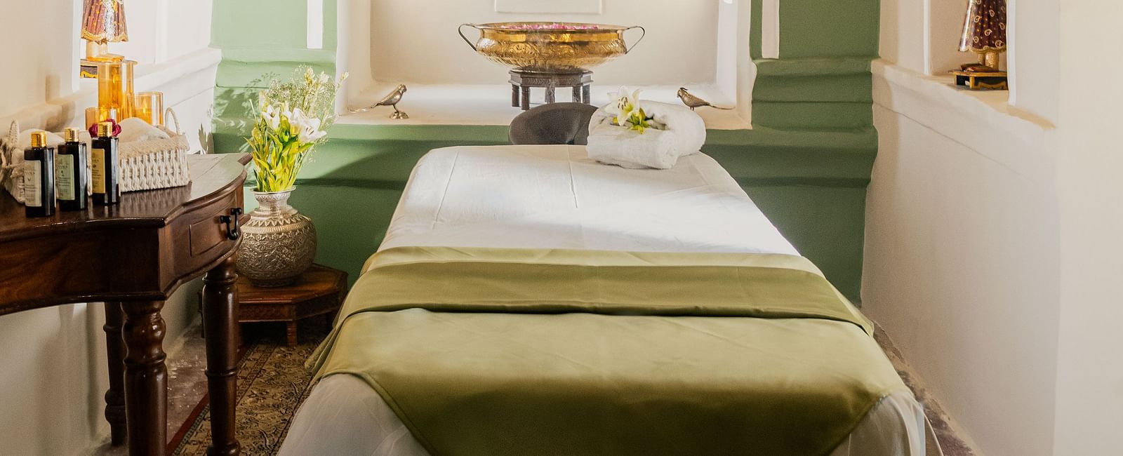 A serene spa treatment room with soft lighting, featuring a massage table, arched alcove, and calming green accents.