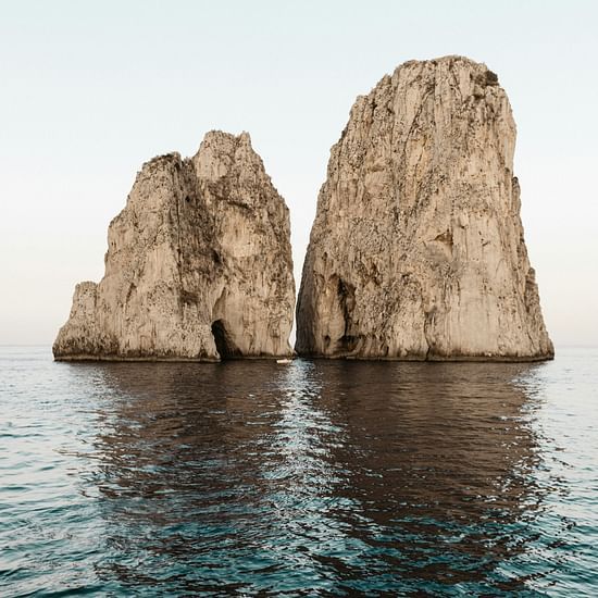 Two towering rock formations rise from the sea, with a natural arch in one of them.