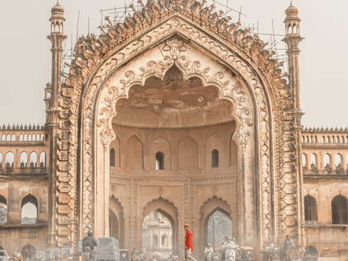 A low-angle view of Lucknow's grand Rumi Darwaza gateway, with a stone path leading towards its ornate, towering arch.