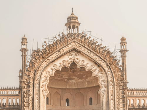 A low-angle view of Lucknow's grand Rumi Darwaza gateway, with a stone path leading towards its ornate, towering arch.