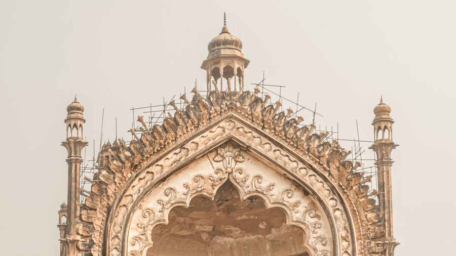 A low-angle view of Lucknow's grand Rumi Darwaza gateway, with a stone path leading towards its ornate, towering arch.