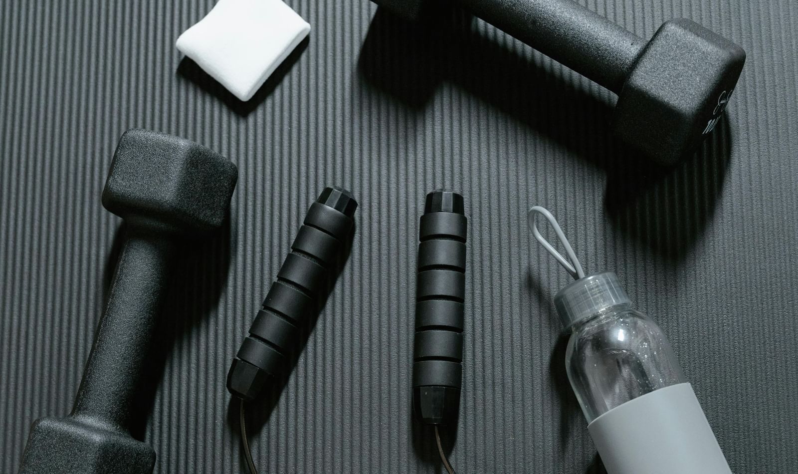 A black jump rope, water bottle and black dumbbells with small white cards placed on the grey surface.