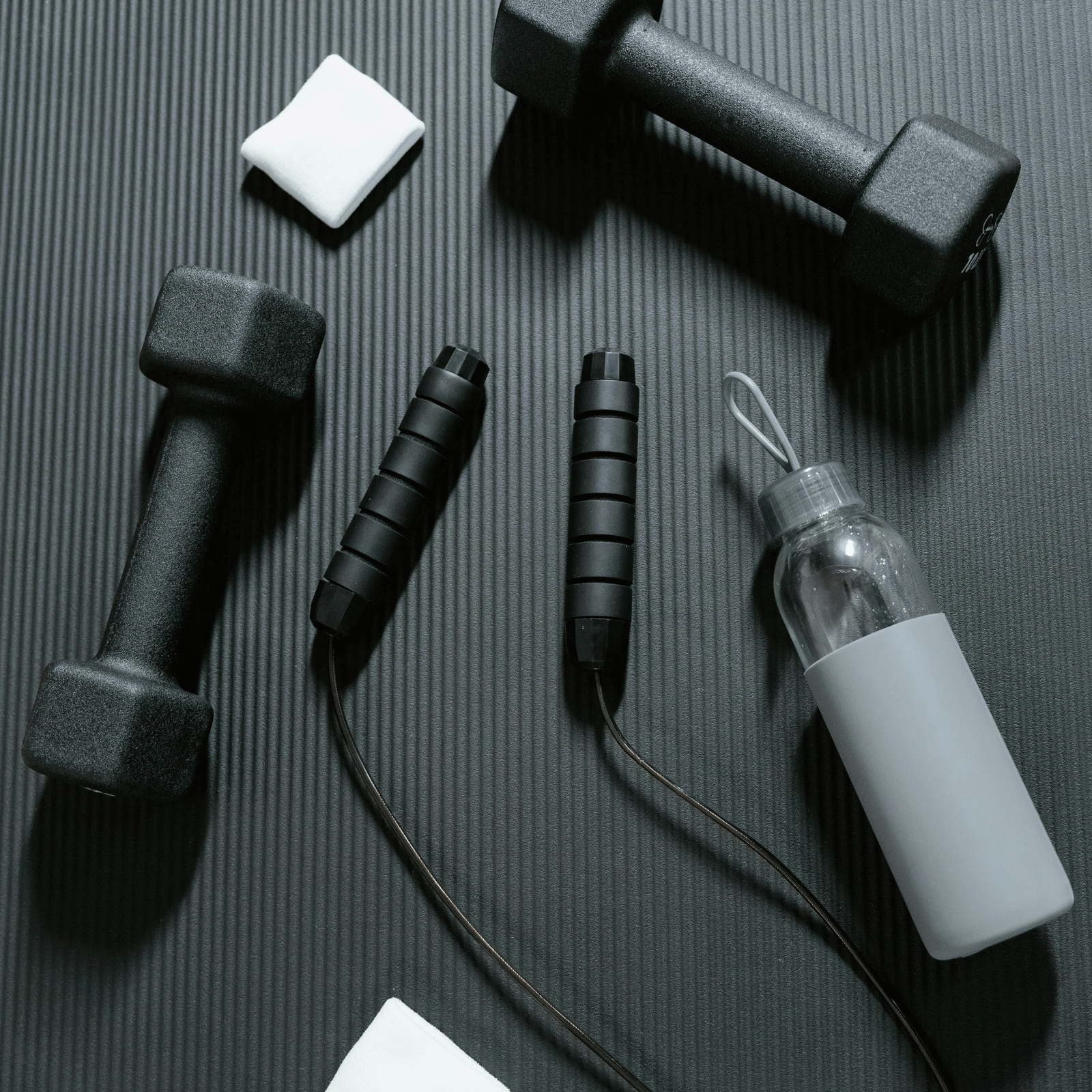 Flatlay of fitness equipment including dumbbells, jump rope, and bottle on a dark surface - Grande Bay Resort & Spa, Mamallapuram