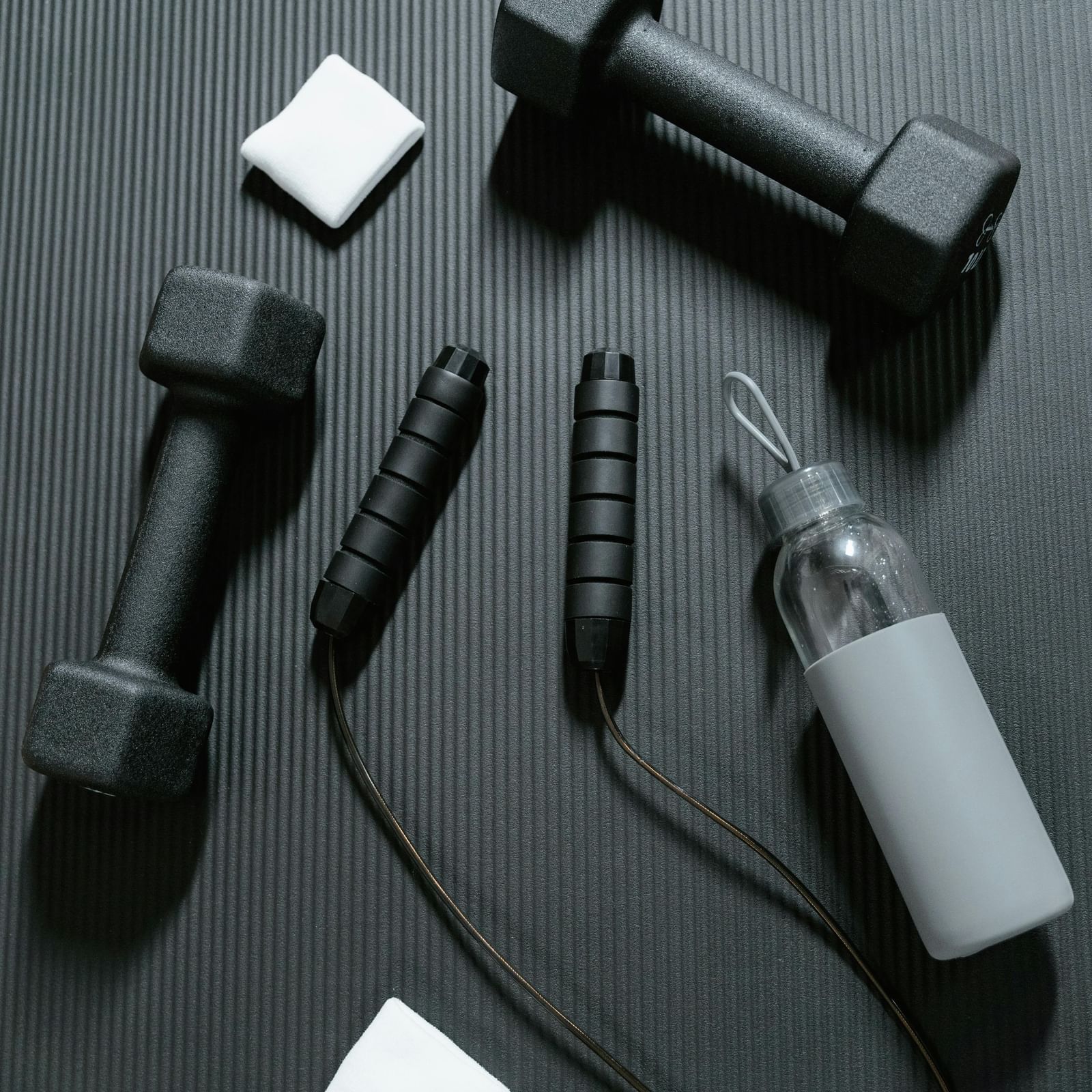 A black jump rope, water bottle and black dumbbells with small white cards placed on the grey surface.
