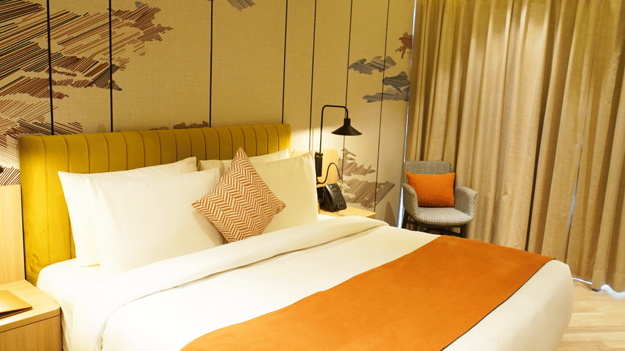 Large bed with cushions and bedside lamps in a stylish room - Ramada Encore by Wyndham Gurugram Dwarka Expressway
