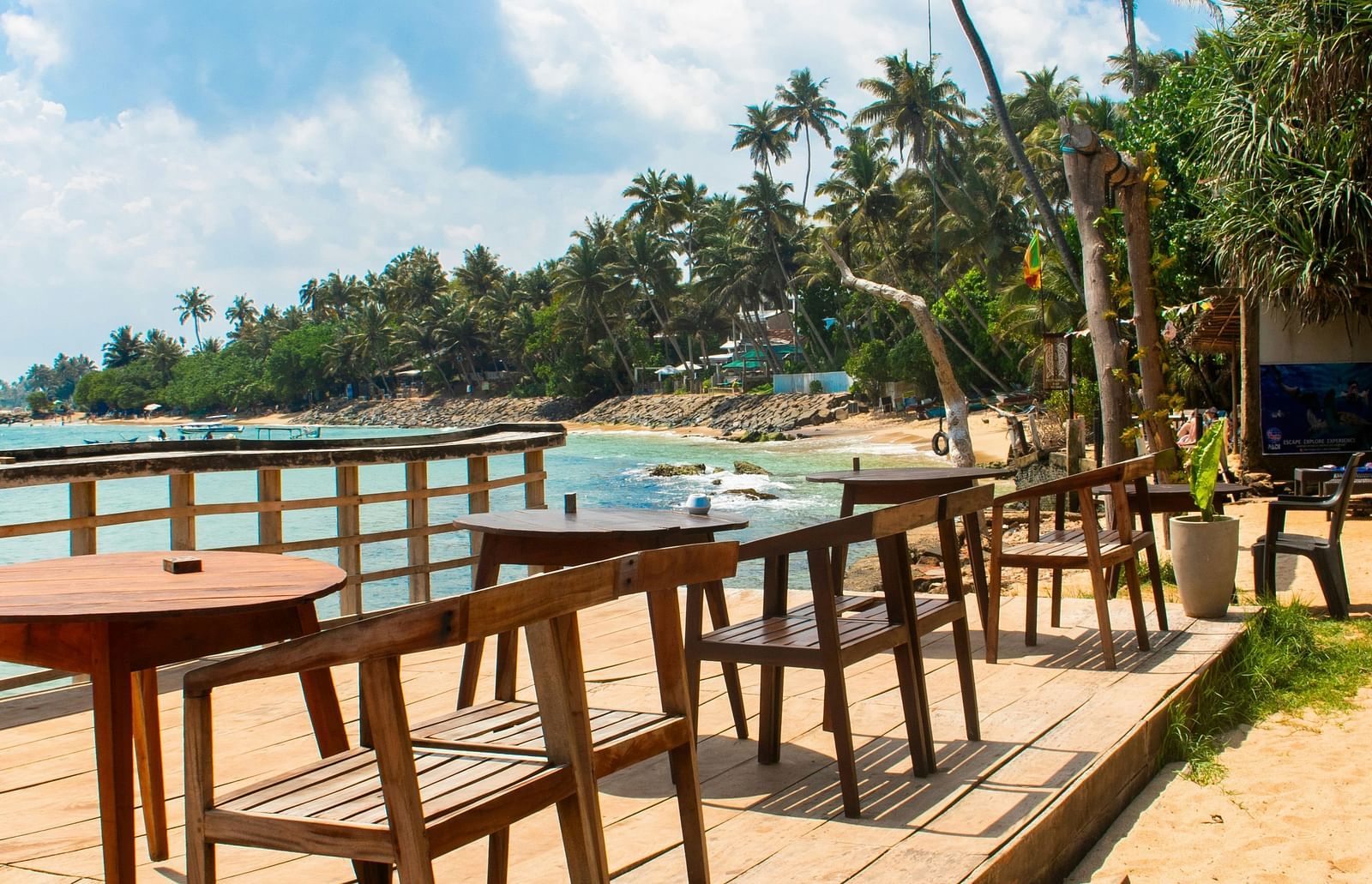 A beachside deck with wooden tables, string lights and palm trees.