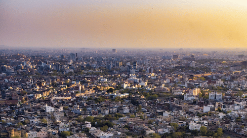 The sun sets over a long fortification wall that follows the ridge of a hill high above the city of Jaipur.