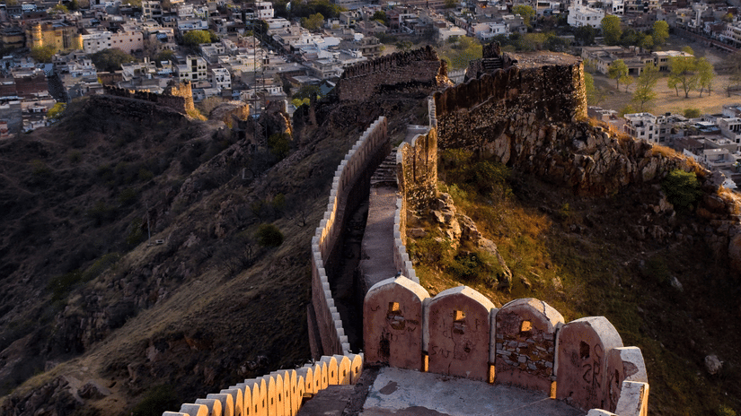 The sun sets over a long fortification wall that follows the ridge of a hill high above the city of Jaipur.