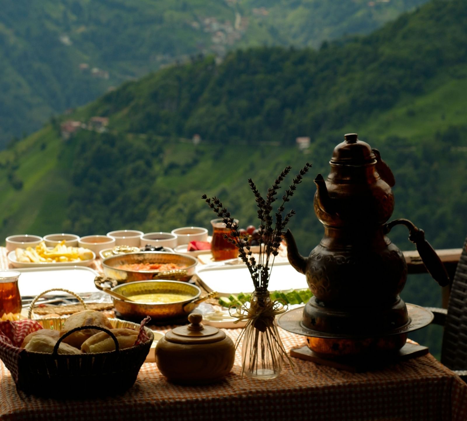 An image of a table where various dishes are placed near a window from where green hills are visible