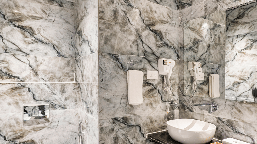 Luxurious hotel bathroom with glass shower, modern fixtures, a deep bathtub, and dramatic green/grey marble walls.