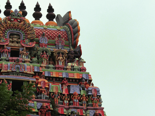 Temple gowpuram with detailed carvings and colourful sculptures rising upward against a light sky background.
