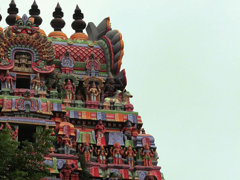 Temple gowpuram with detailed carvings and colourful sculptures rising upward against a light sky background.