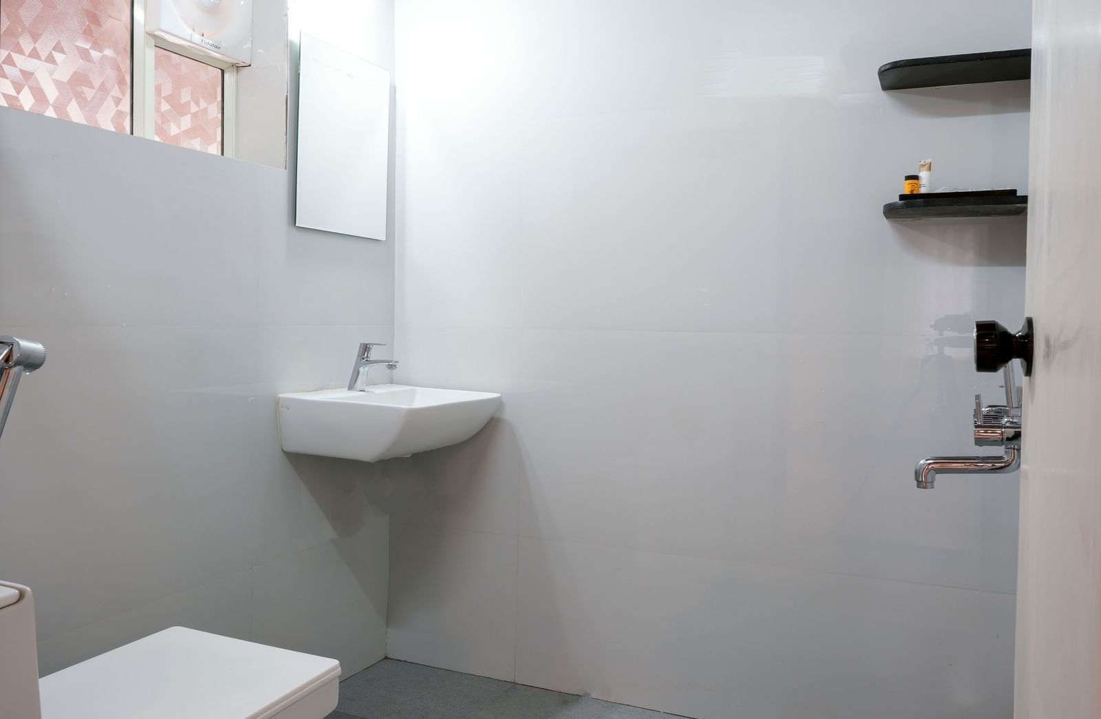 A modern and clean en-suite bathroom at Bhuthanakadu Retreat, showcasing a simple sink, a toilet, and a tiled shower area with minimal and functional design.
