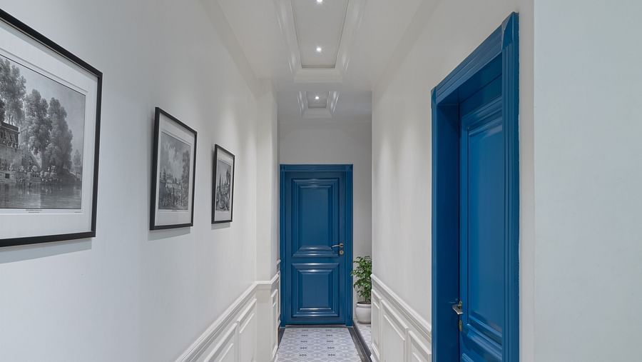 A corridor has a wall-mounted frame on one side and doors on the other side | Hotel Ganga Maiya