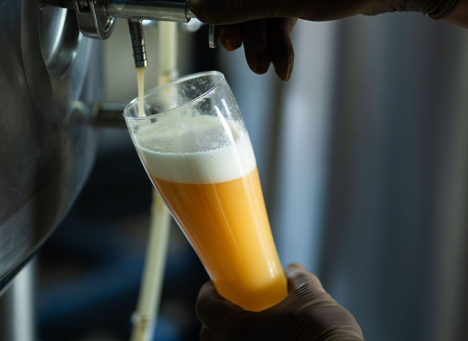 A close-up shows a bartender's hand pouring beer from a tap into a glass, highlighting the brewing process at The Qualia Resort Club & Brewery, Udaipur.