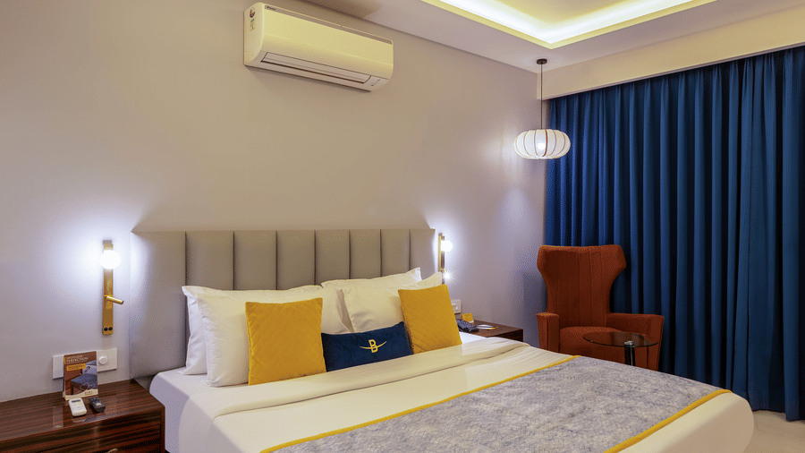 Standard suite interior featuring a stylish orange armchair, side table, and double bed with warm lighting.