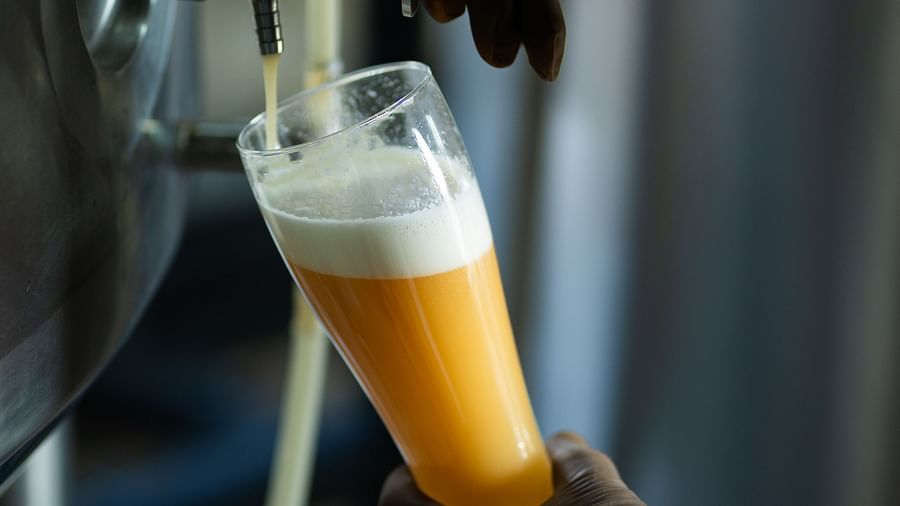 A close-up shows a bartender's hand pouring beer from a tap into a glass, highlighting the brewing process at The Qualia Resort Club & Brewery, Udaipur.