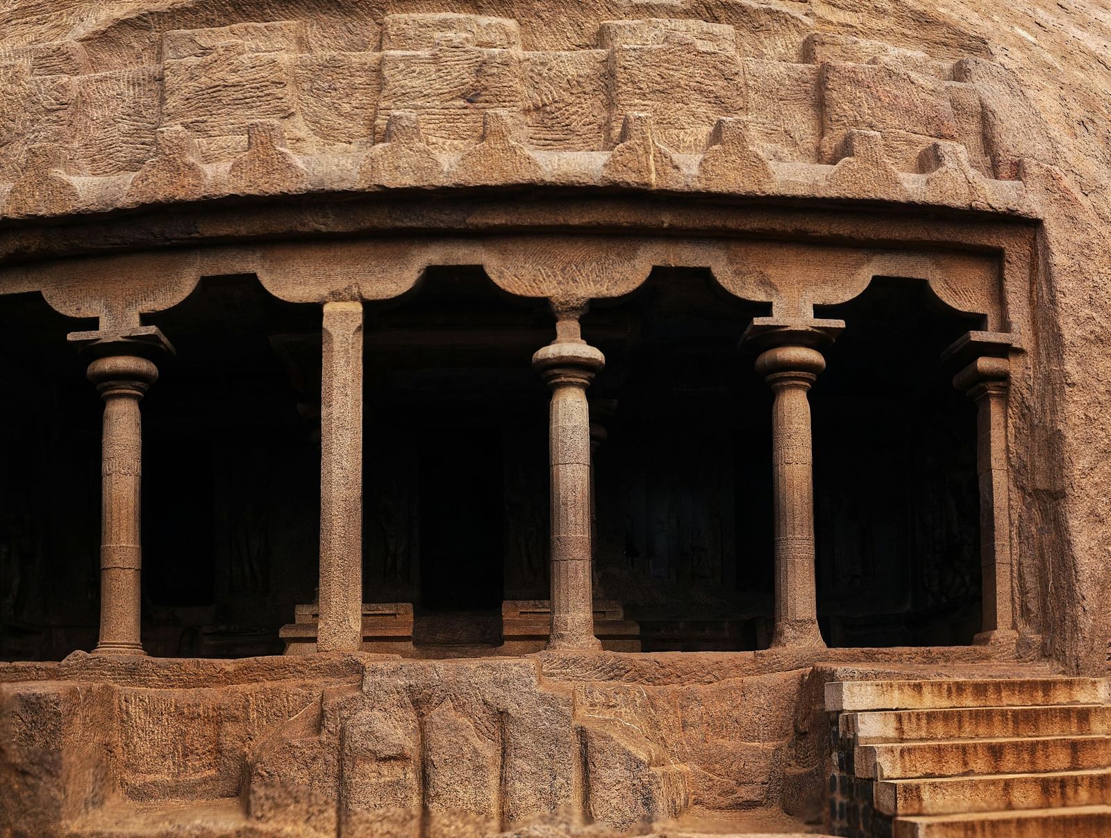 A dark, ancient cave temple entrance with carved windows and worn stone steps leading up.