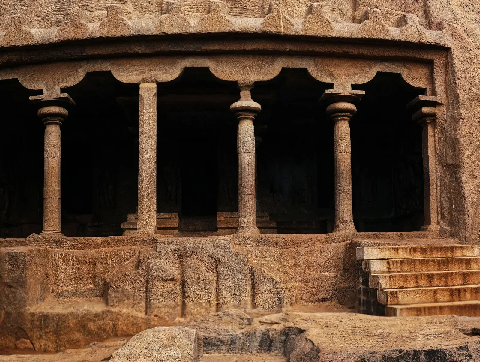 A dark, ancient cave temple entrance with carved windows and worn stone steps leading up.