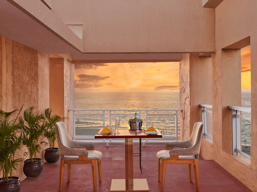 Open terrace dining setup at The Resort, Mumbai overlooking the sea during sunset, with a table for two, warm lighting, and coastal views creating a relaxed ambience.