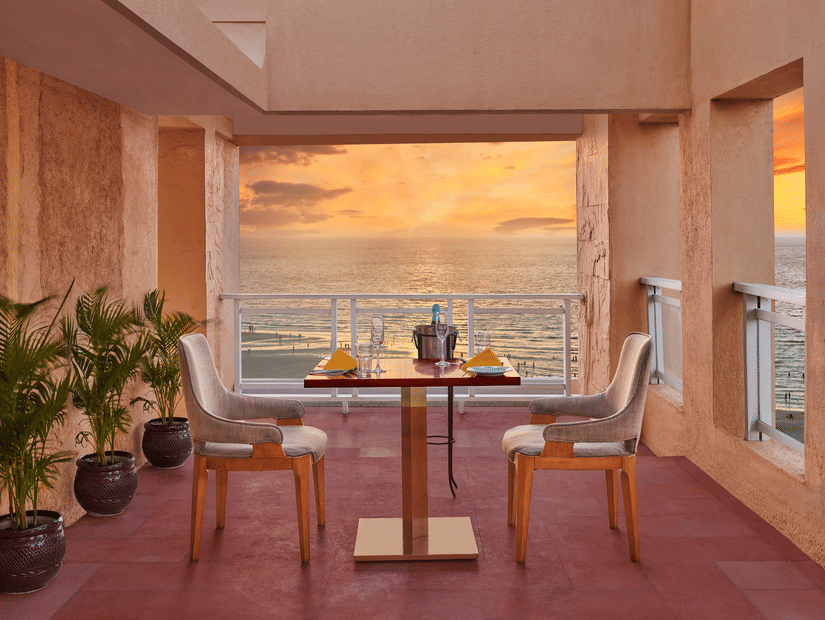 Open terrace dining setup at The Resort, Mumbai overlooking the sea during sunset, with a table for two, warm lighting, and coastal views creating a relaxed ambience.