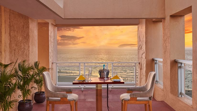 A balcony with a table set for two, overlooking the ocean at sunset - The Resort, Mumbai.