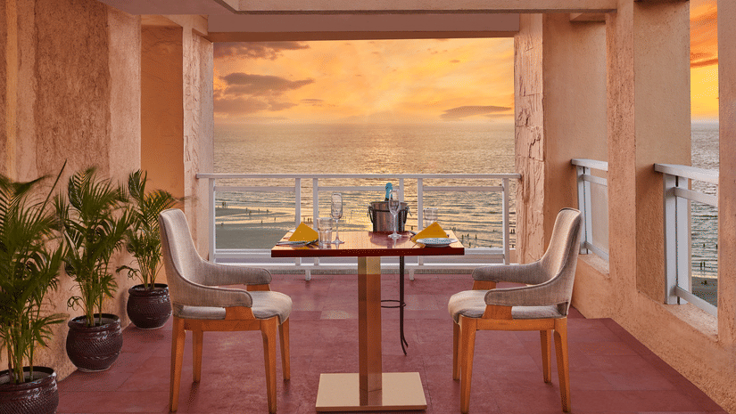 Open terrace dining setup at The Resort, Mumbai overlooking the sea during sunset, with a table for two, warm lighting, and coastal views creating a relaxed ambience.