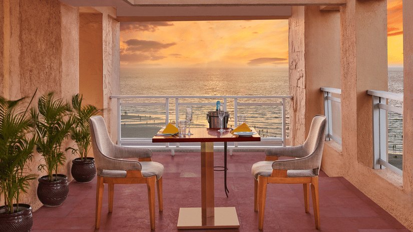 Open terrace dining setup at The Resort, Mumbai overlooking the sea during sunset, with a table for two, warm lighting, and coastal views creating a relaxed ambience.